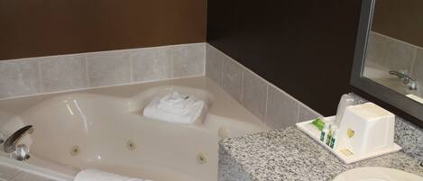Un baño con una bañera grande, encimera de granito, lavabo y espejo.