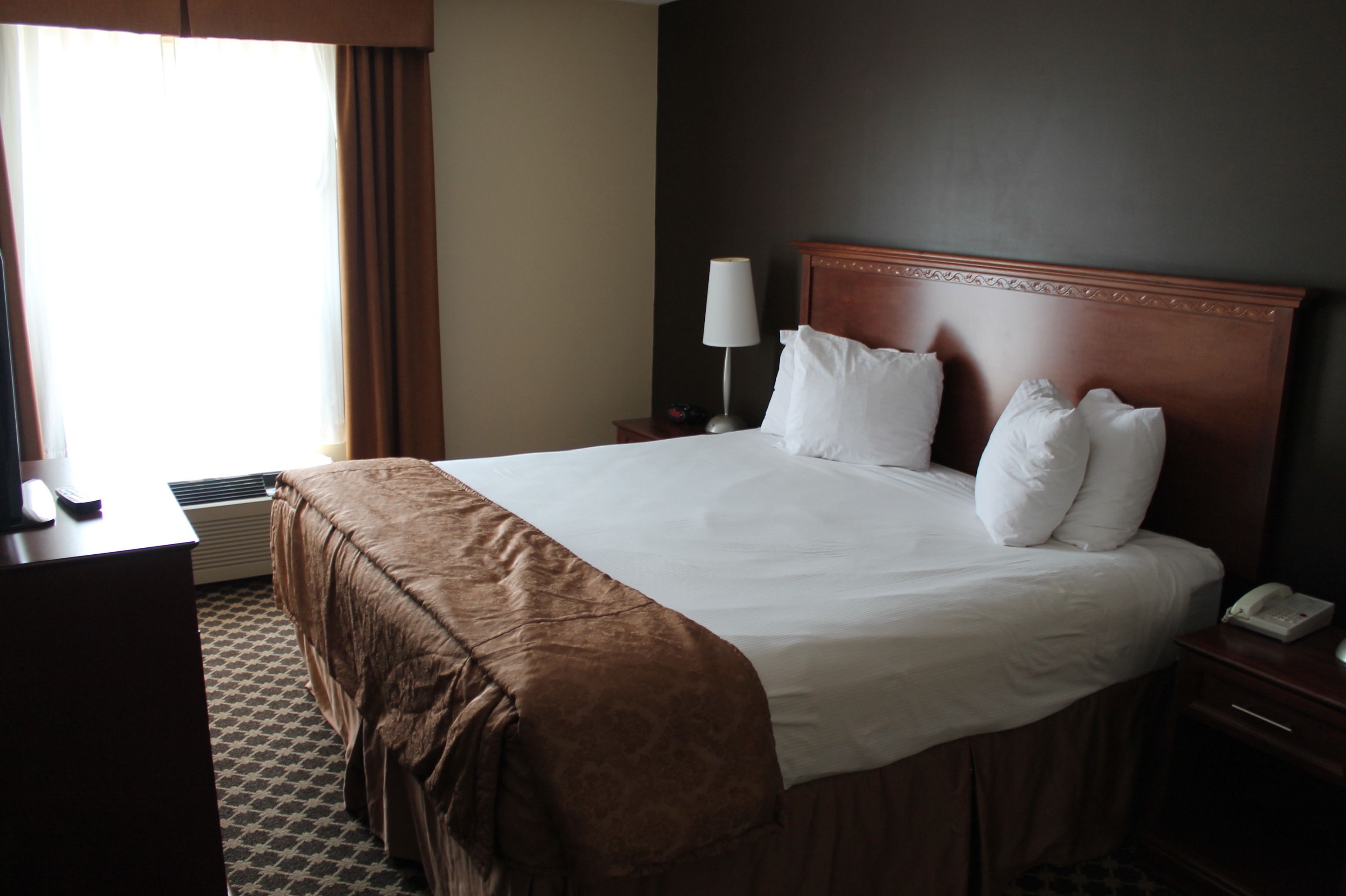 A hotel room with a large bed, a bedside lamp, a telephone, and a window with curtains.