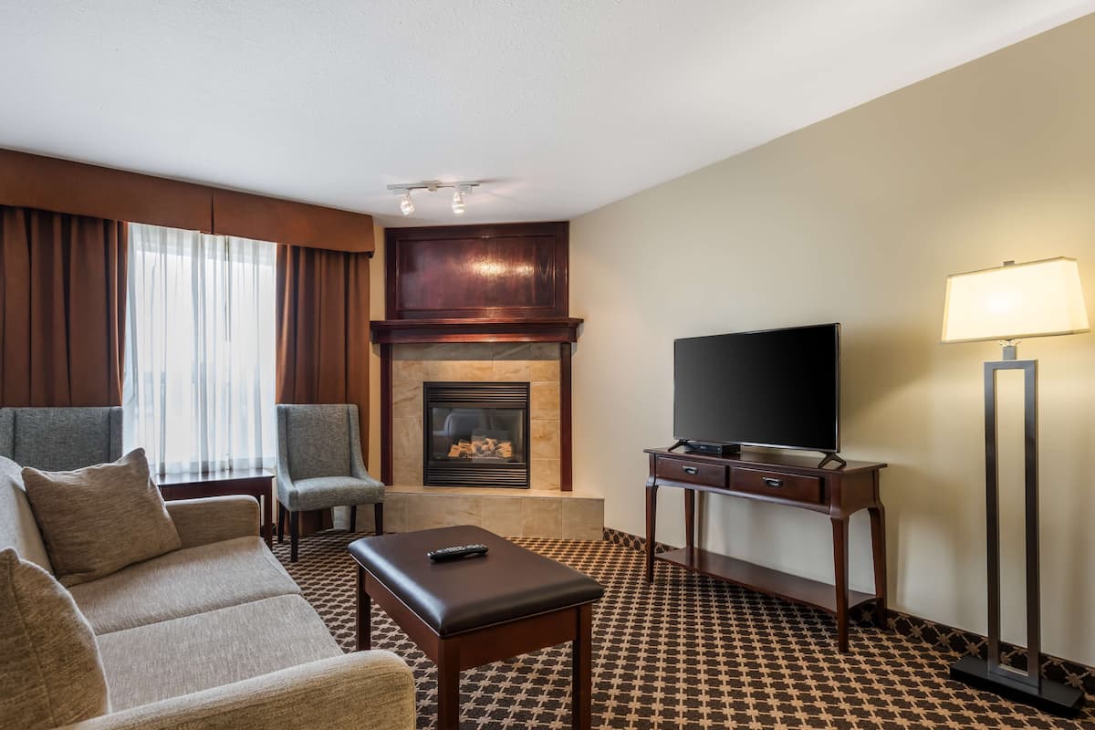 Ein Hotelzimmer mit einer Couch, zwei Sesseln, einem Flachbildfernseher, einem Kamin, einer Lampe und einem gemusterten Teppich.