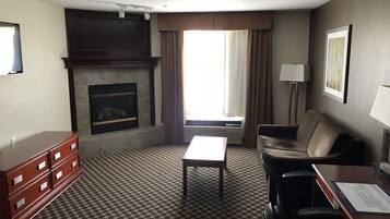 A hotel room with a fireplace, a sofa, a coffee table, a desk with a chair, and a patterned carpet.