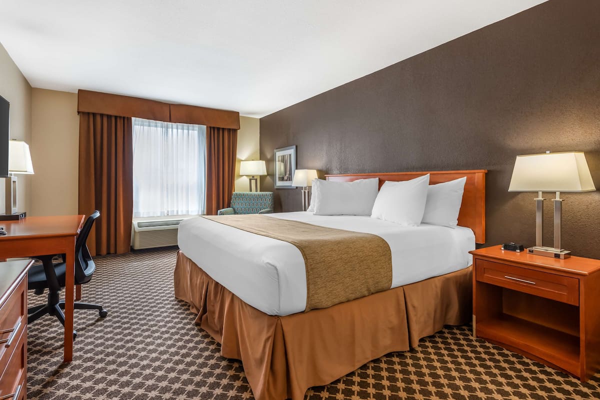 Ein Hotelzimmer mit einem großen Bett, einem Schreibtisch, einem Sessel, einer Kommode und einem Fenster mit Vorhängen.