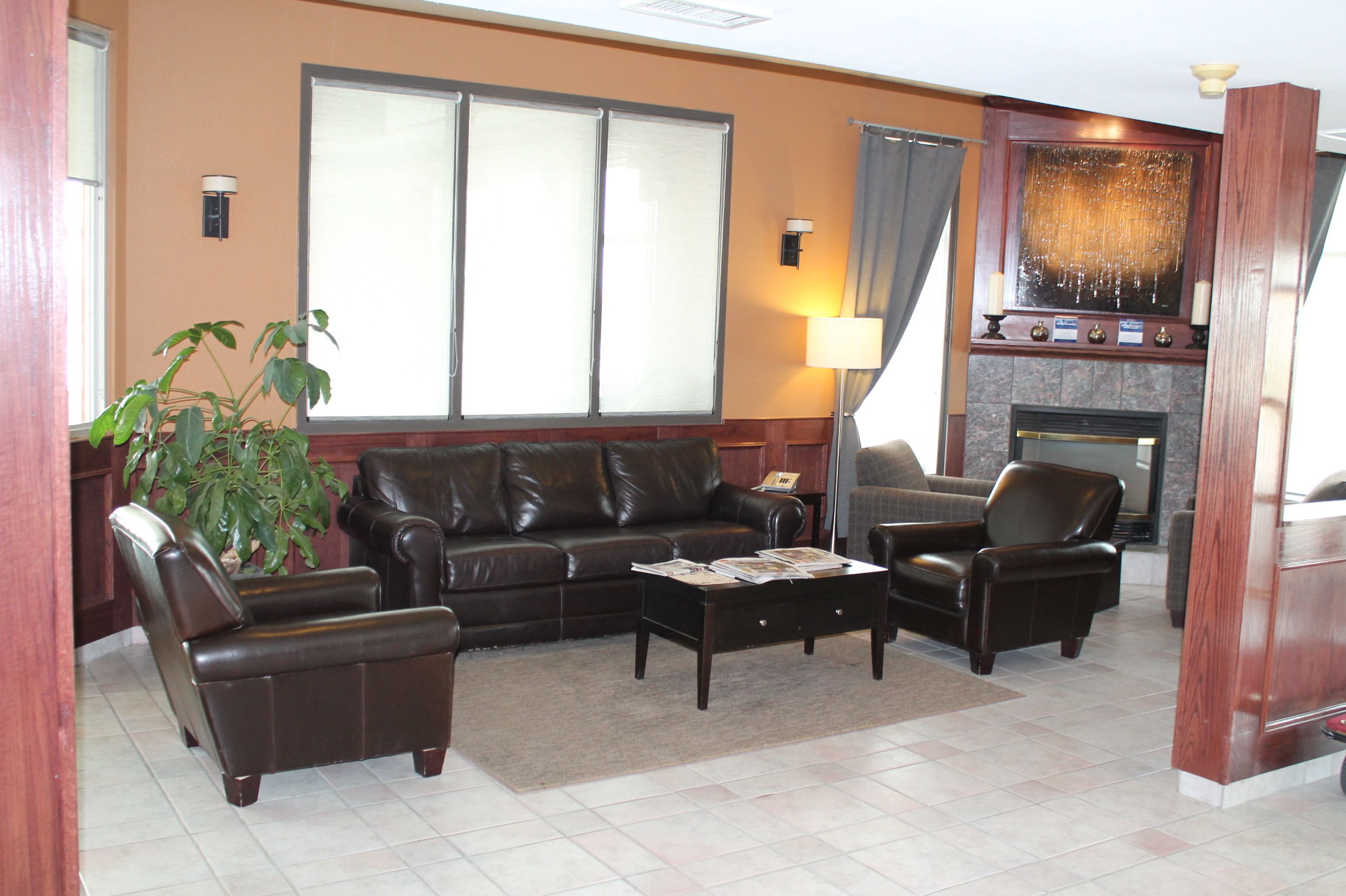 Ein Wohnzimmer mit braunem Ledersofa, zwei Sesseln, einem Couchtisch, einem Kamin und einem großen Fenster mit Jalousien.