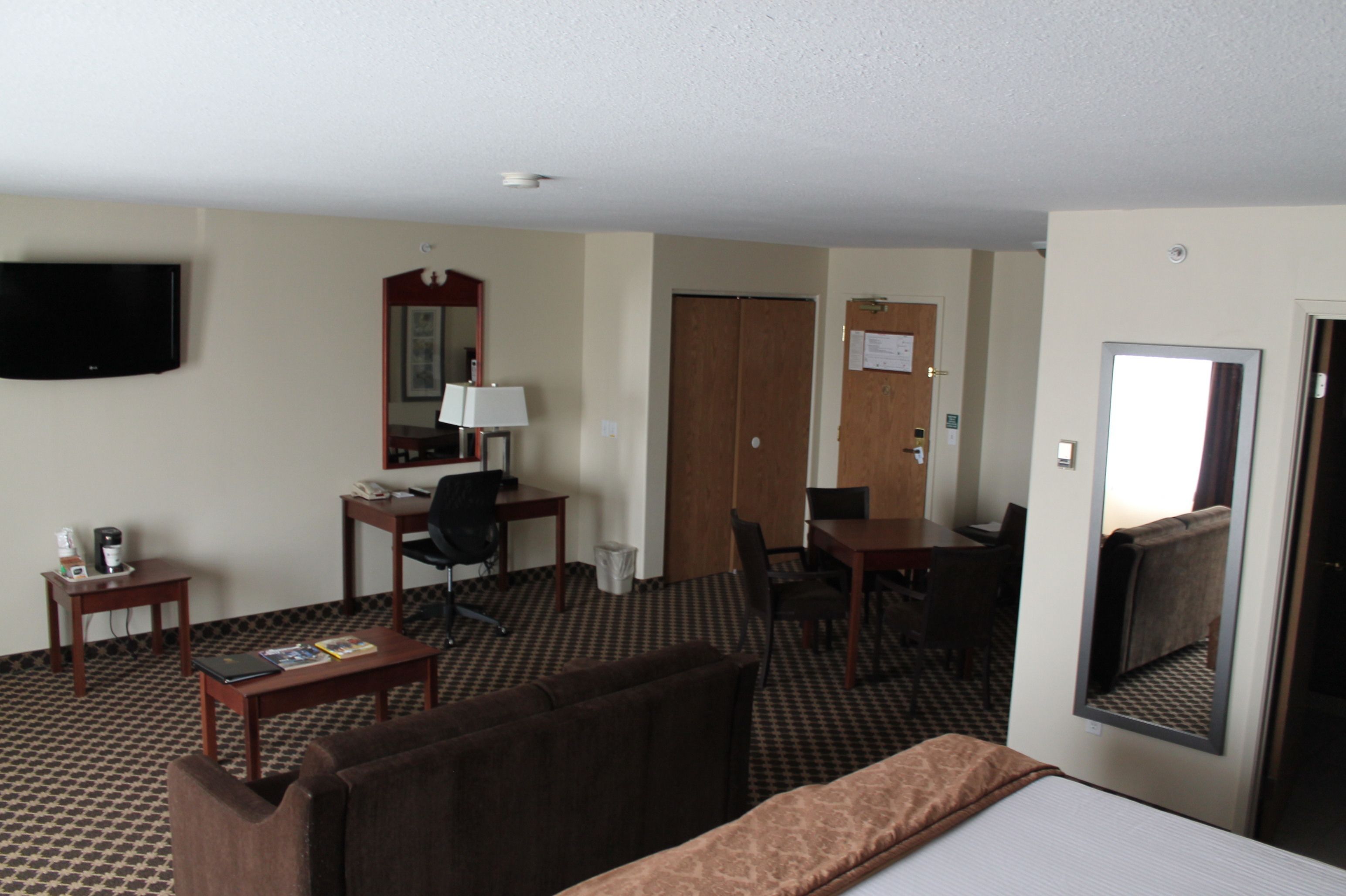 A hotel room with a bed, a desk, a chair, a TV, and a mirror.