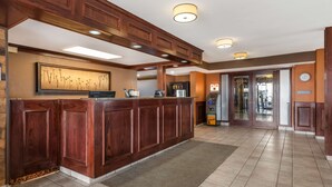 A reception area with a wooden reception desk, a framed floral artwork, a clock, and an ATM. - Best Western Strathmore Inn (Strathmore)