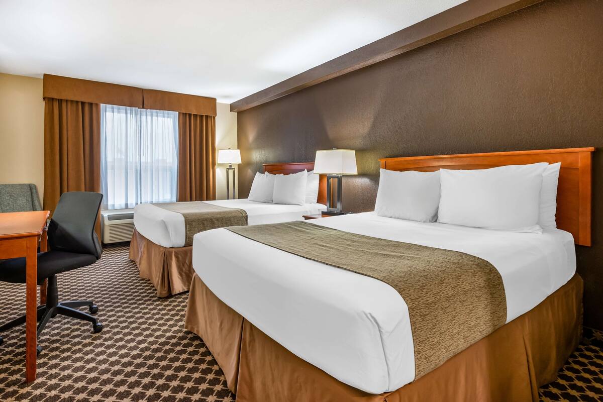 Ein Hotelzimmer mit zwei Betten, einem Schreibtisch, einem Stuhl und einem Fenster mit Vorhängen.