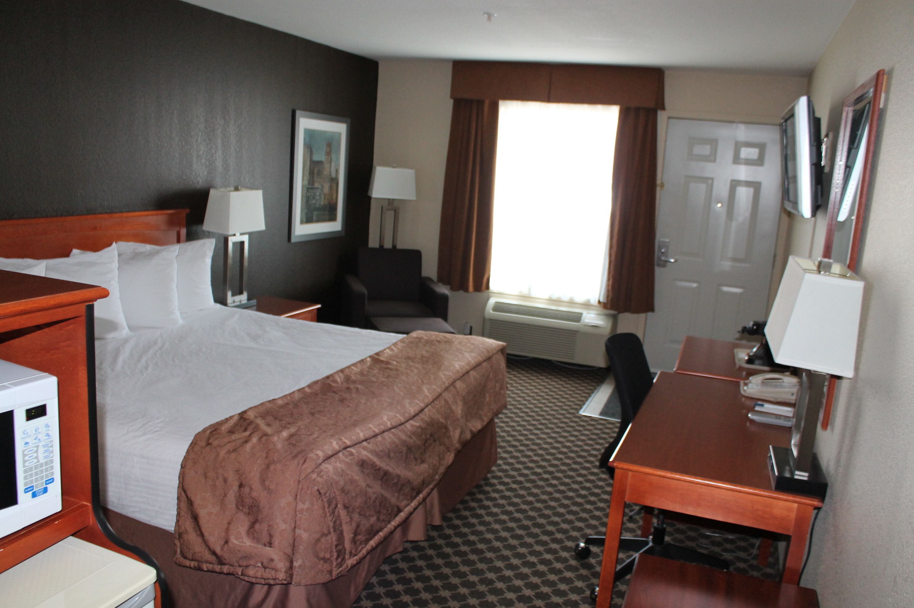 A hotel room with a bed, desk, chair, and a microwave.