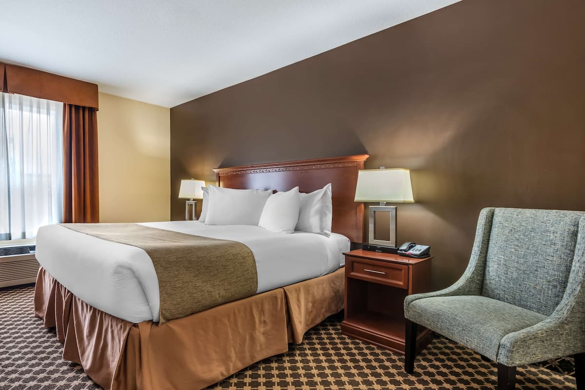 Ein Hotelzimmer mit einem großen Bett, zwei Nachttischen mit Lampen, einem Sessel und einem Fernseher.