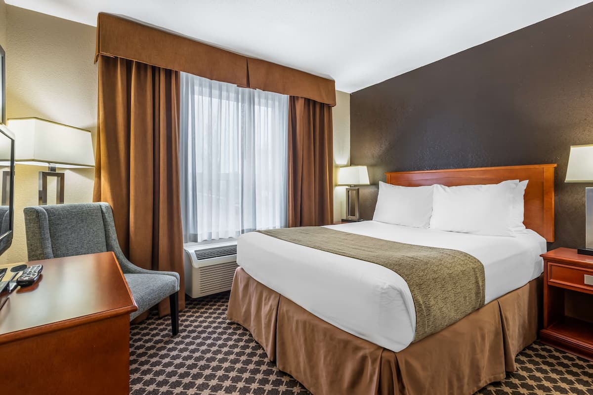 Ein Hotelzimmer mit einem großen Bett, einem Schreibtisch mit Stuhl, einem Fernseher und einem Fenster mit Vorhängen.
