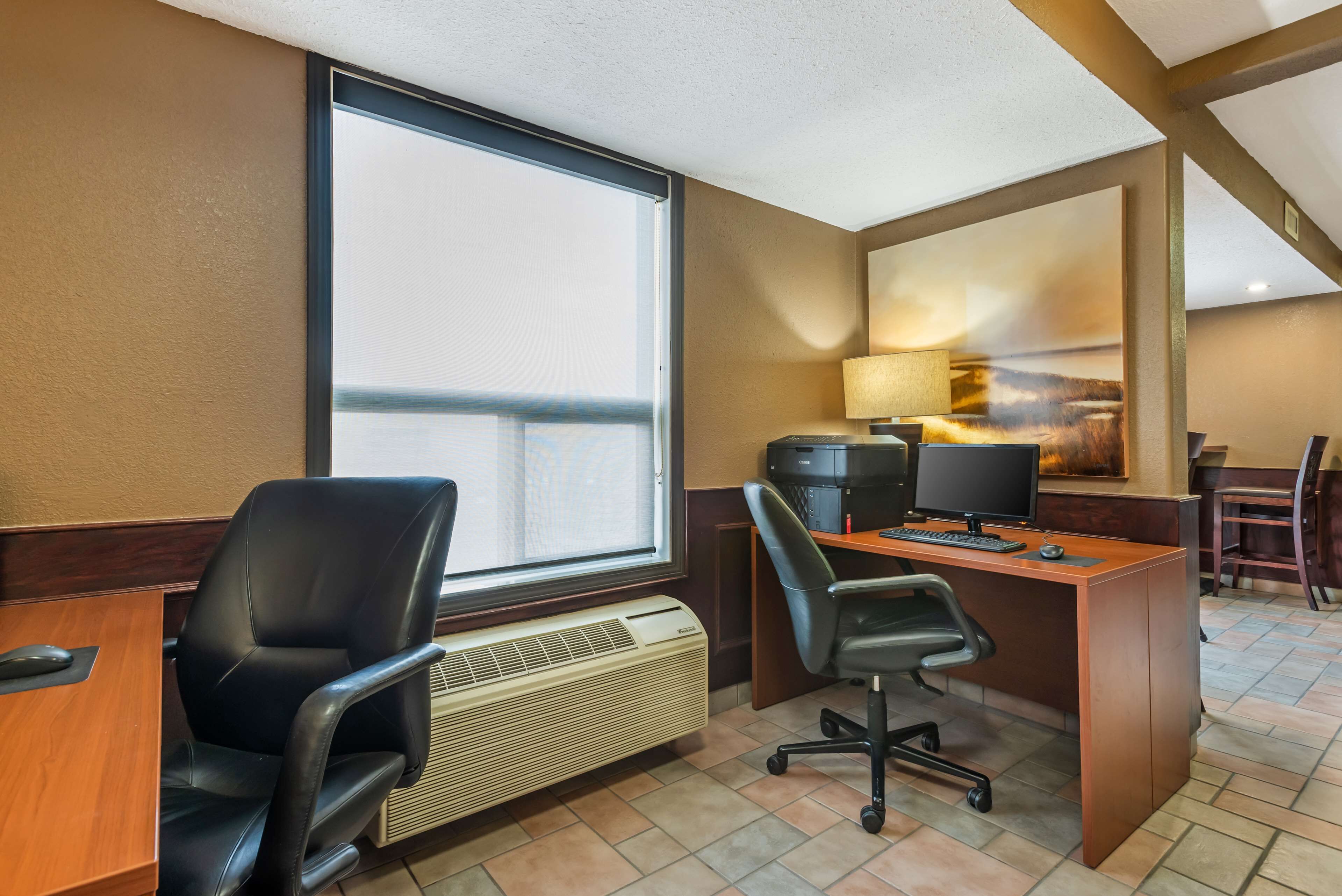 Un bureau d’hôtel avec une grande fenêtre, un bureau équipé d’un ordinateur, une chaise et un radiateur.