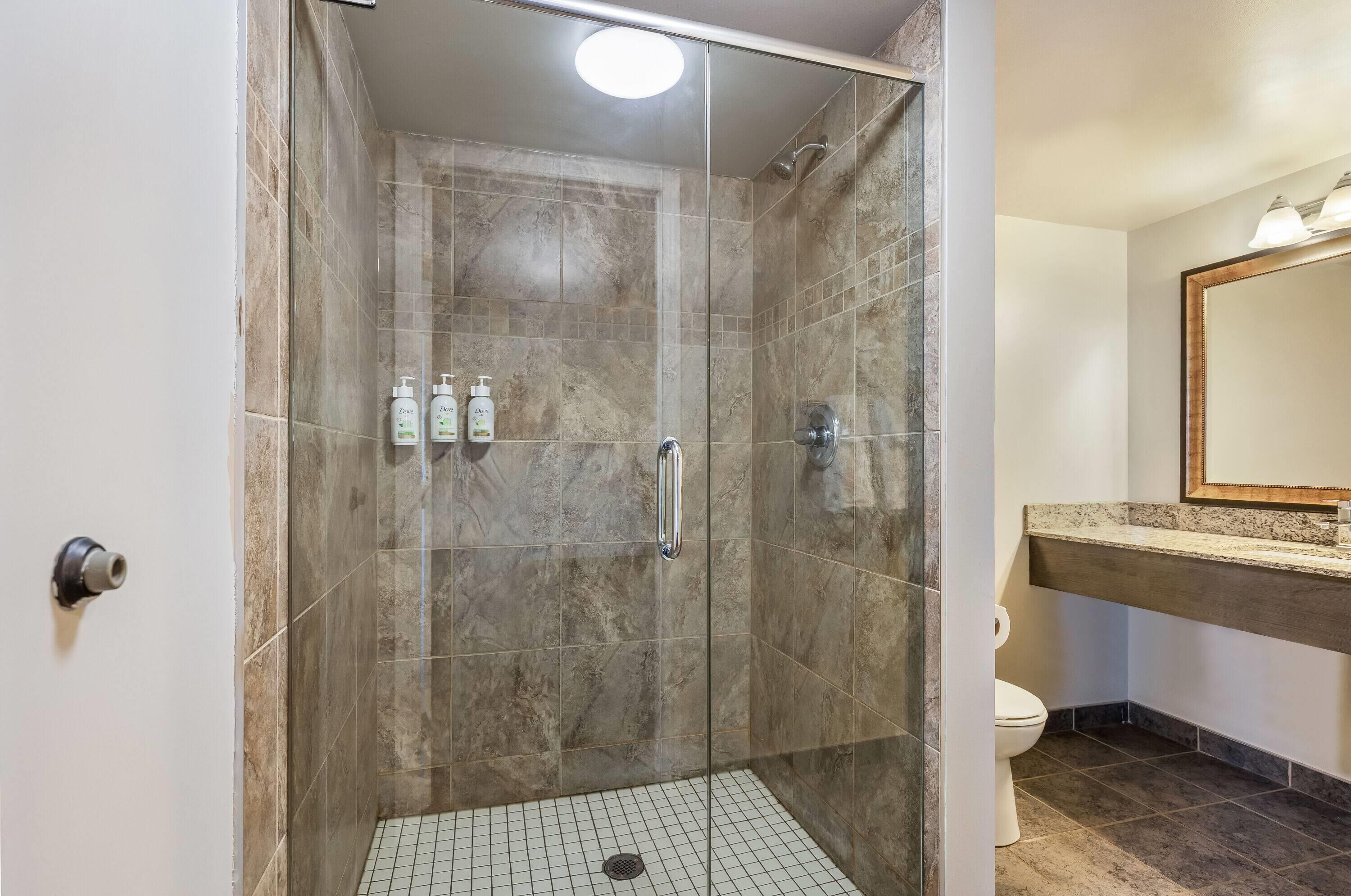 A shower with a glass door, a tiled floor, and a toilet in the adjacent bathroom.