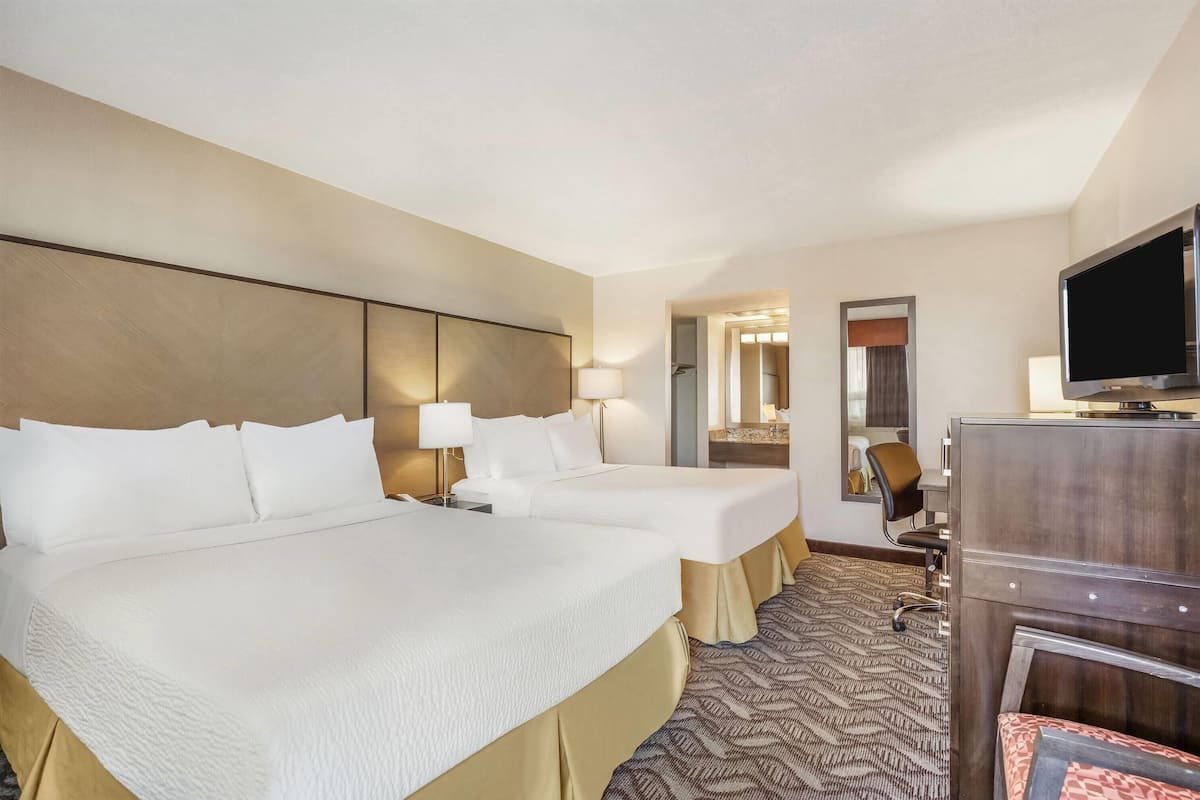 A hotel room with two beds, a TV, a desk, and a mirror.