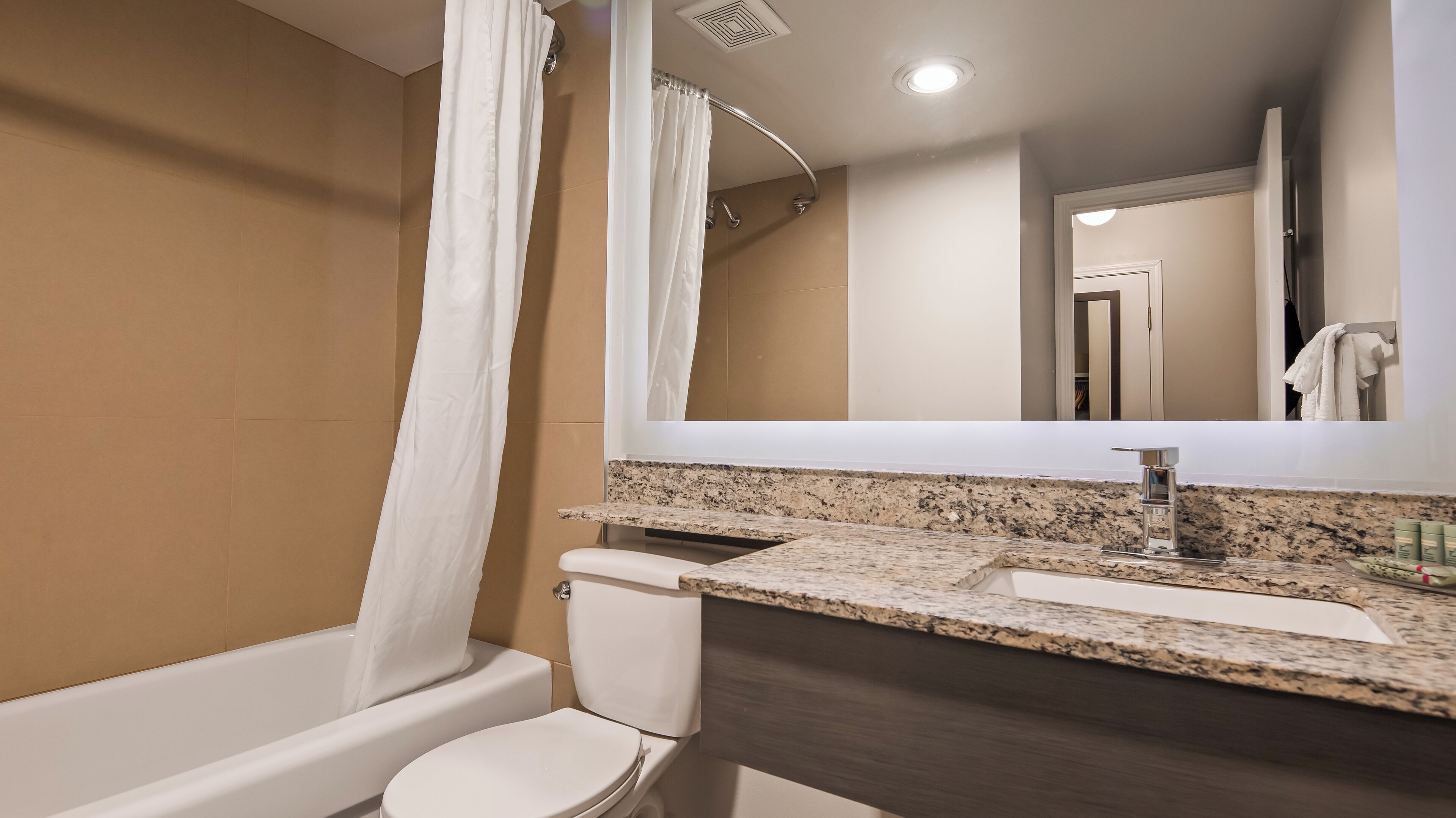 A modern bathroom with a bathtub, toilet, and a large mirror above a granite countertop.