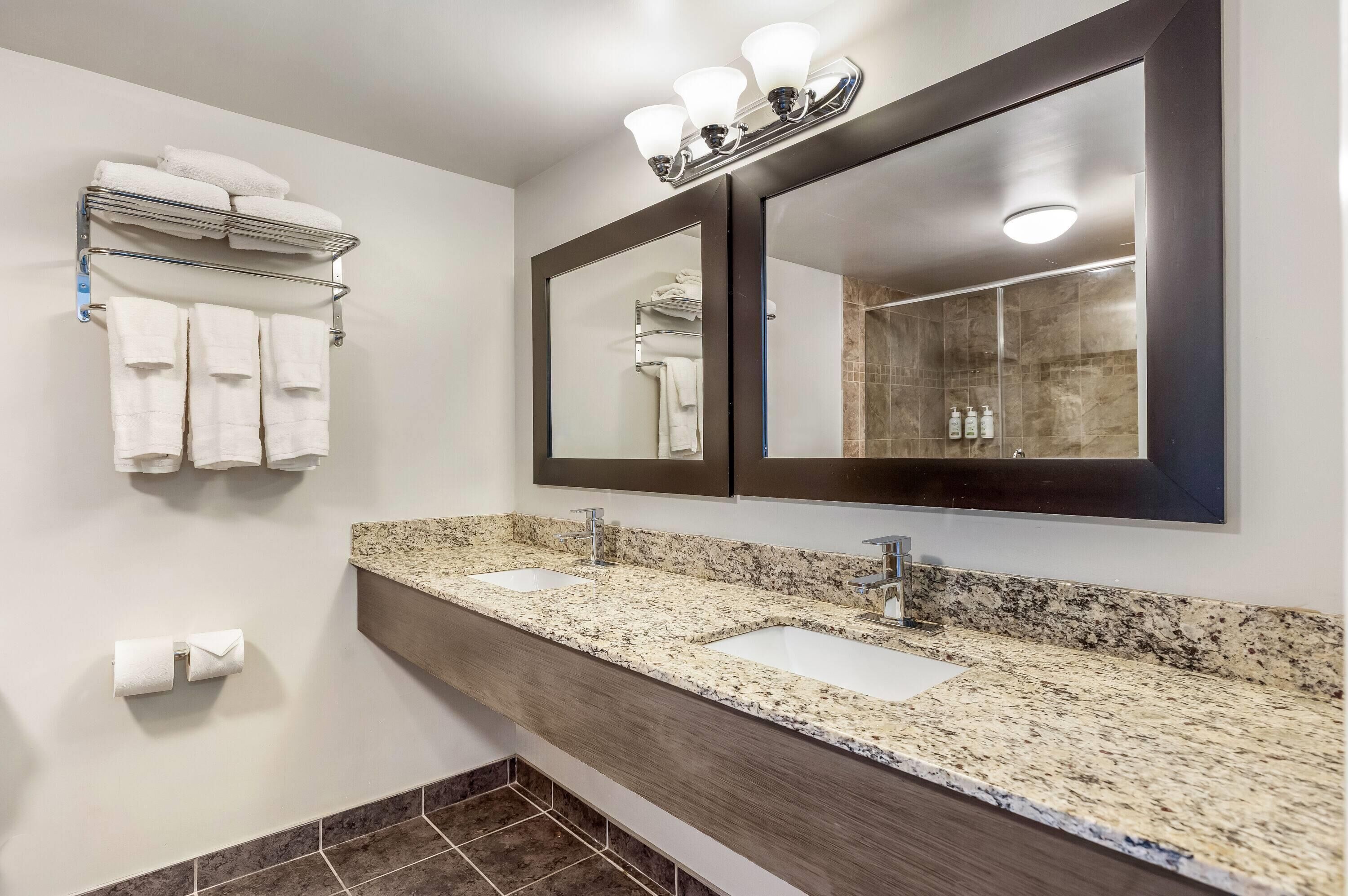 Une salle de bain avec deux lavabos, un grand miroir et un porte-serviettes avec des serviettes pliées.