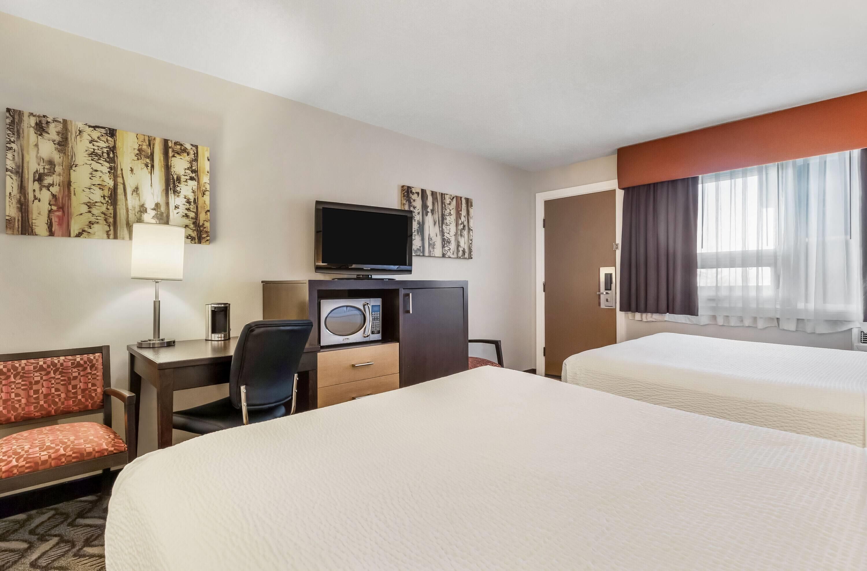 A hotel room with two beds, a desk with a TV, a microwave, and a chair.