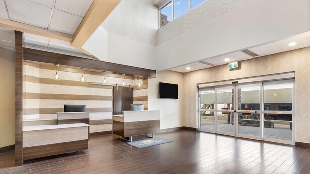 A modern reception area with a wooden reception desk, a flat-screen TV, and a glass door entrance. - Days Inn by Wyndham Airdrie (Airdrie)