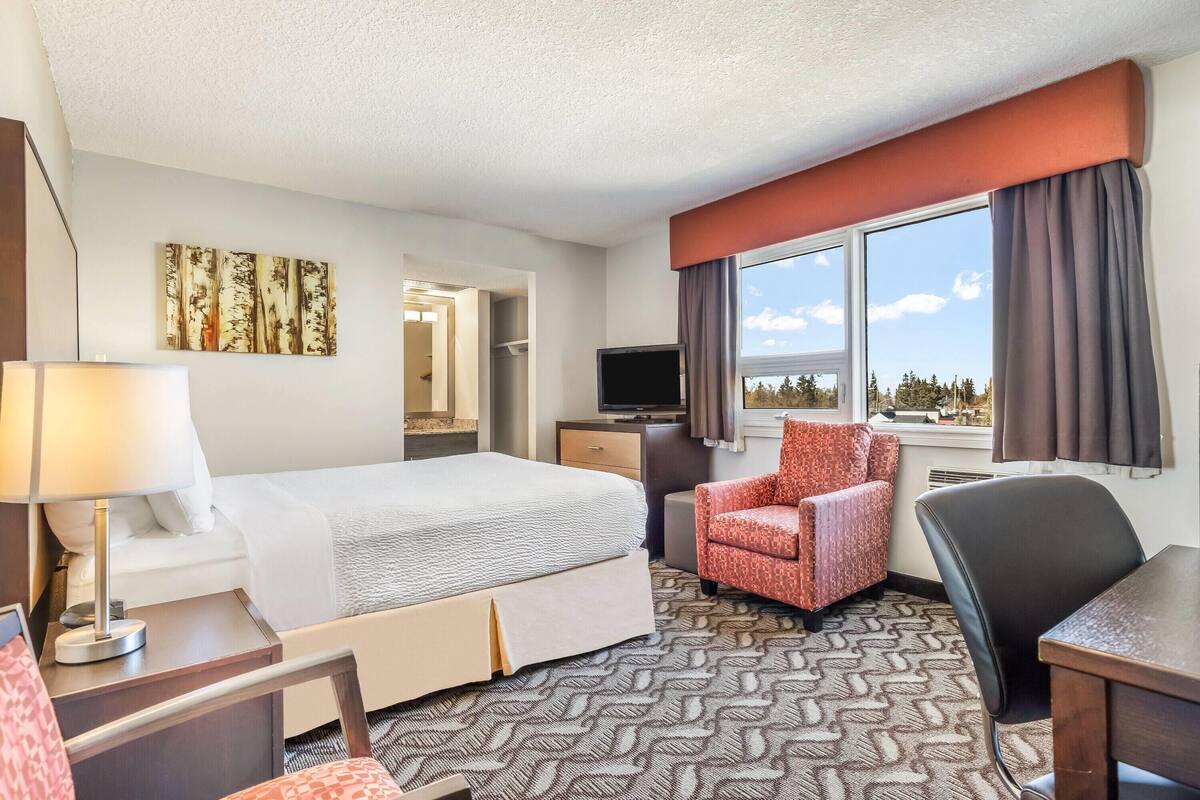 A hotel room with a bed, a desk, a chair, a television, and a window with curtains.