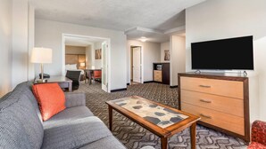 A hotel room with a sofa, a coffee table, a TV, a dresser, and a carpeted floor. - Days Inn by Wyndham Airdrie (Airdrie)