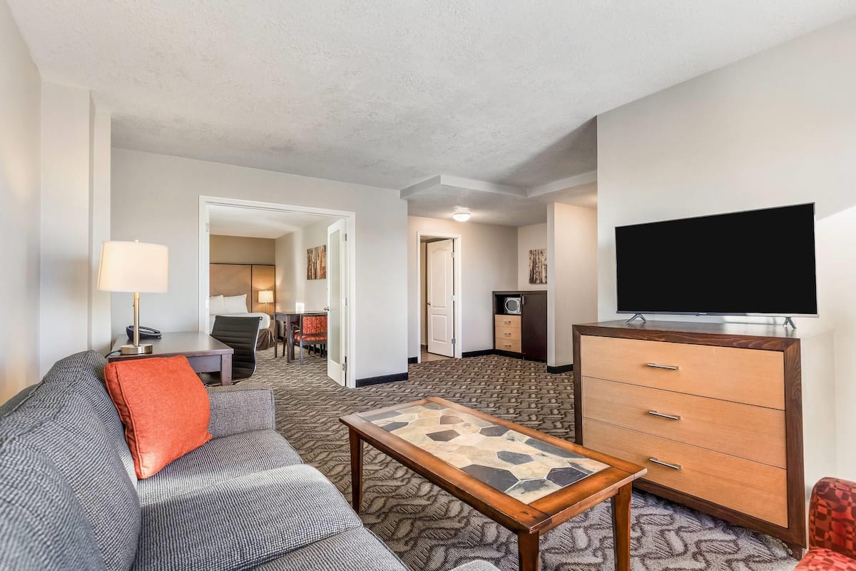 A hotel room with a sofa, a coffee table, a TV, a dresser, and a carpeted floor.