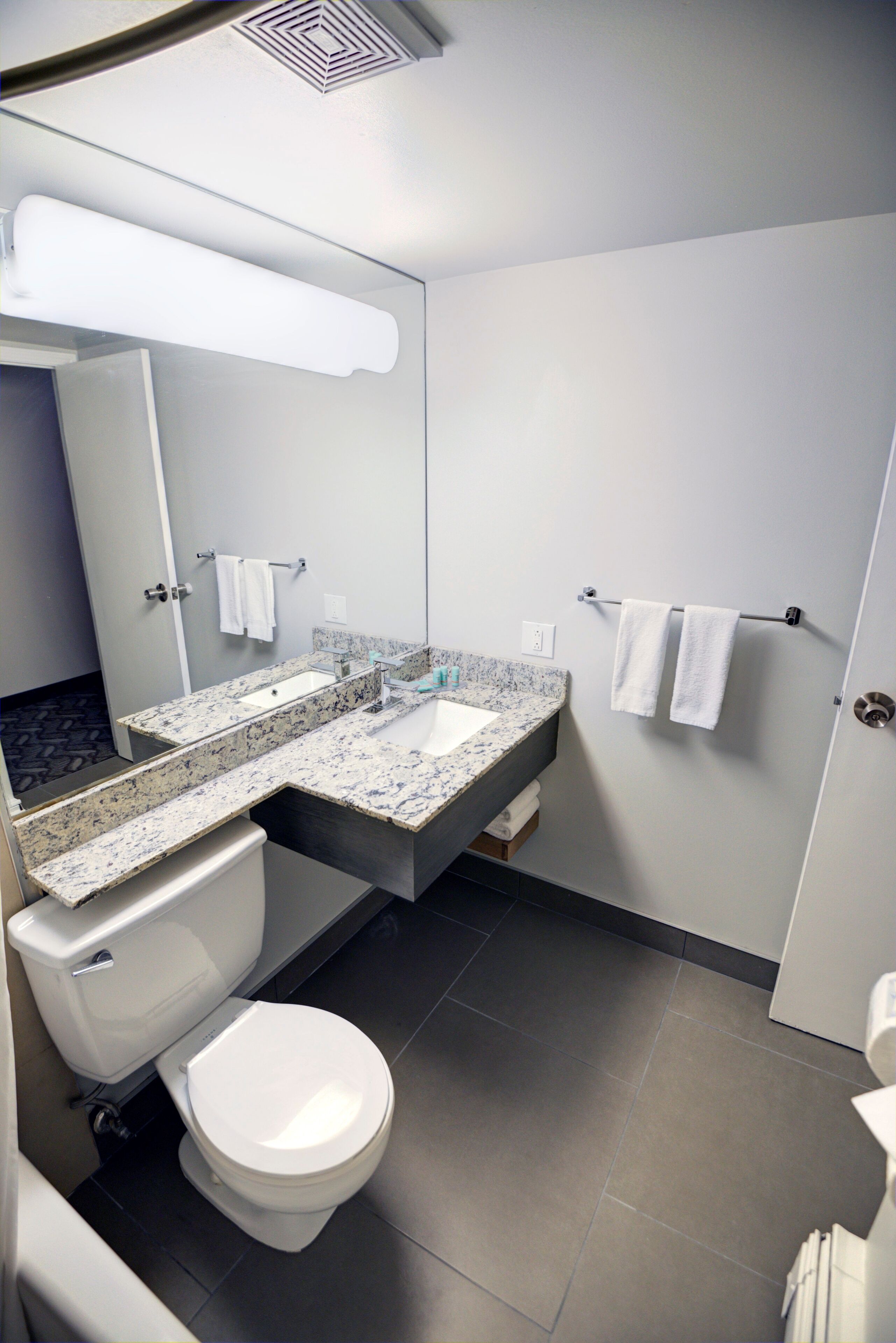 A modern bathroom with a white toilet, a granite countertop sink, and a large mirror.