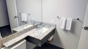 A modern bathroom with a white toilet, a granite countertop sink, and a large mirror.