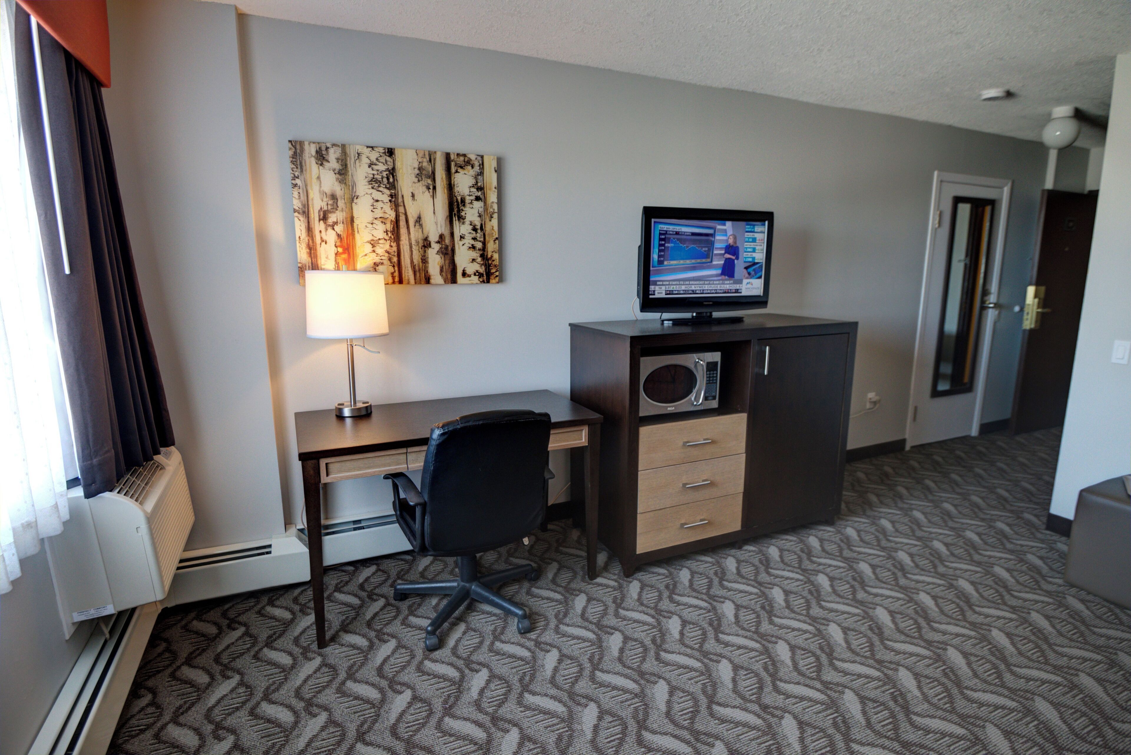 A hotel room with a desk, chair, television, and a patterned carpet.