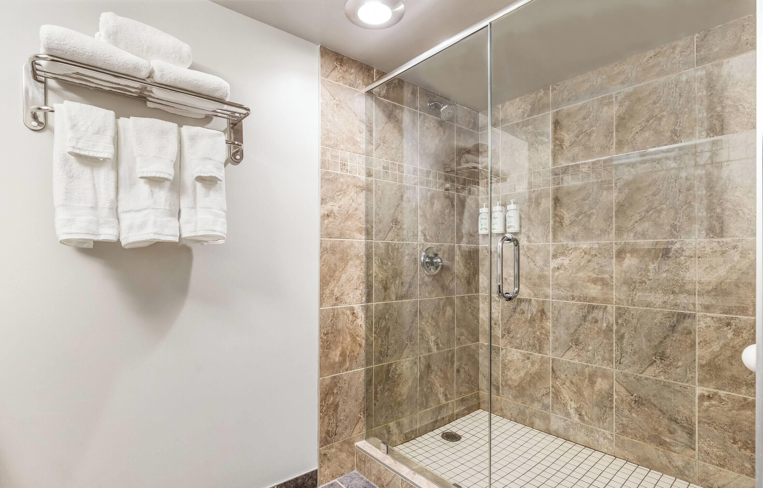 A shower with a glass door, a towel rack with multiple towels, and a tiled wall.