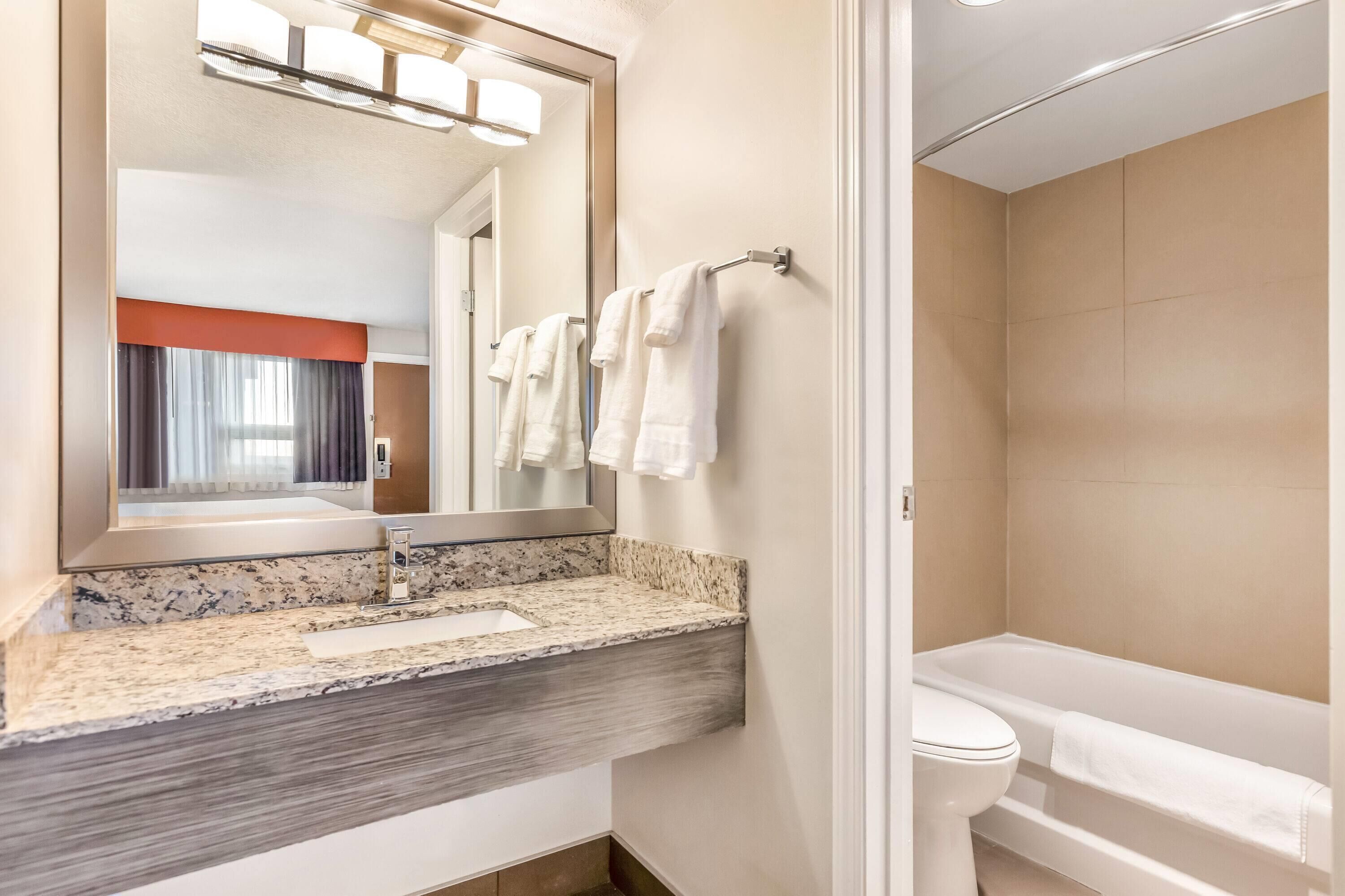A modern bathroom with a granite countertop, a large mirror, a towel rack, and a bathtub.