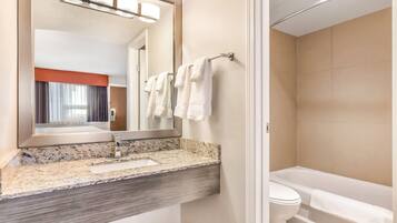 A modern bathroom with a granite countertop, a large mirror, a towel rack, and a bathtub.