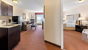 A hotel room with a kitchenette, a living area with a sofa and coffee table, a bed with a headboard, and a bathroom with a bathtub. - Best Western Of Olds (Olds)