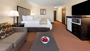 A hotel room with a bed, a sofa, a coffee table with apples, a TV, a mini-fridge, and a microwave. - Best Western Of Olds (Olds)
