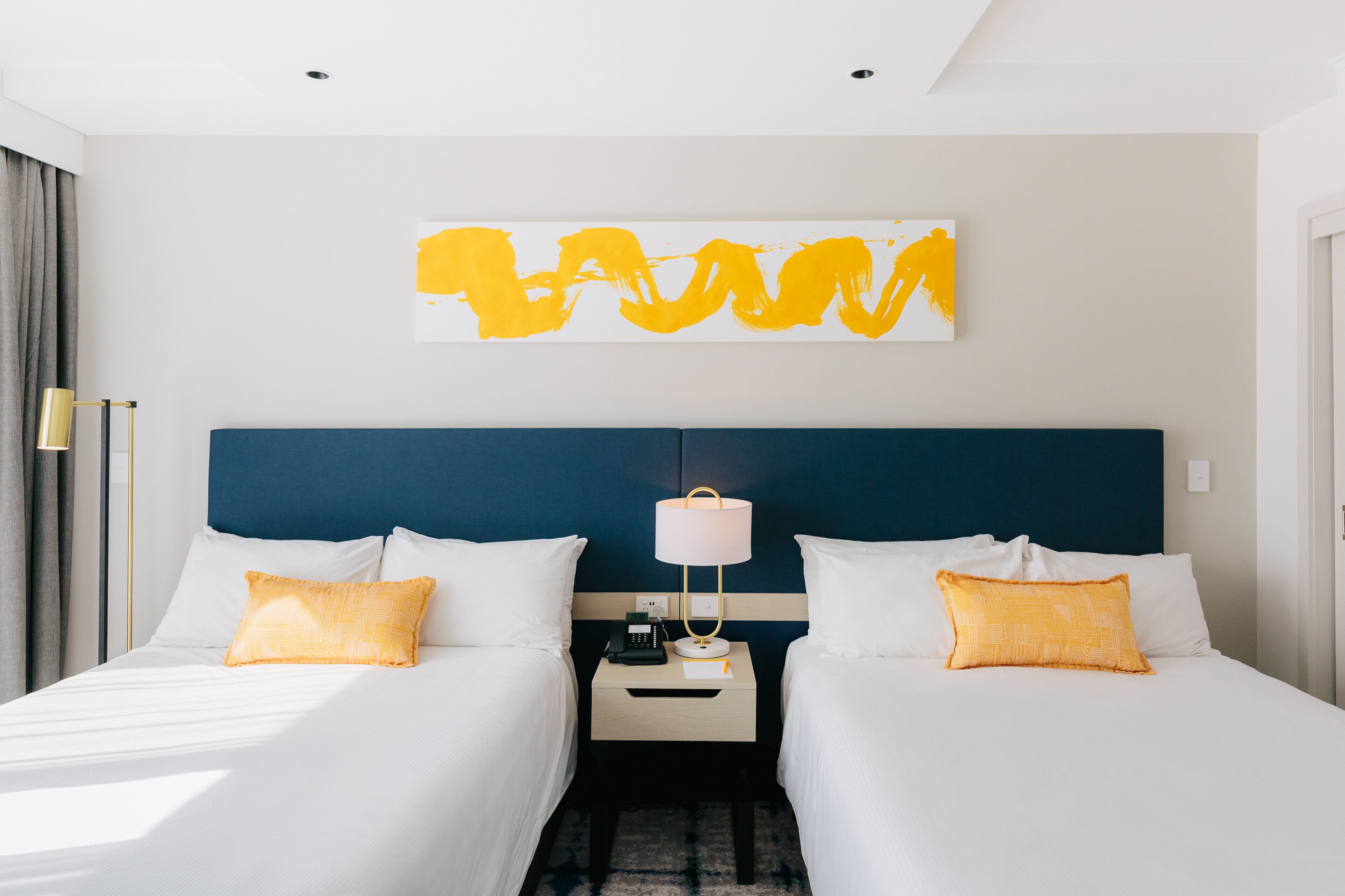 A hotel room with two beds, a nightstand with a lamp, and a wall art piece.