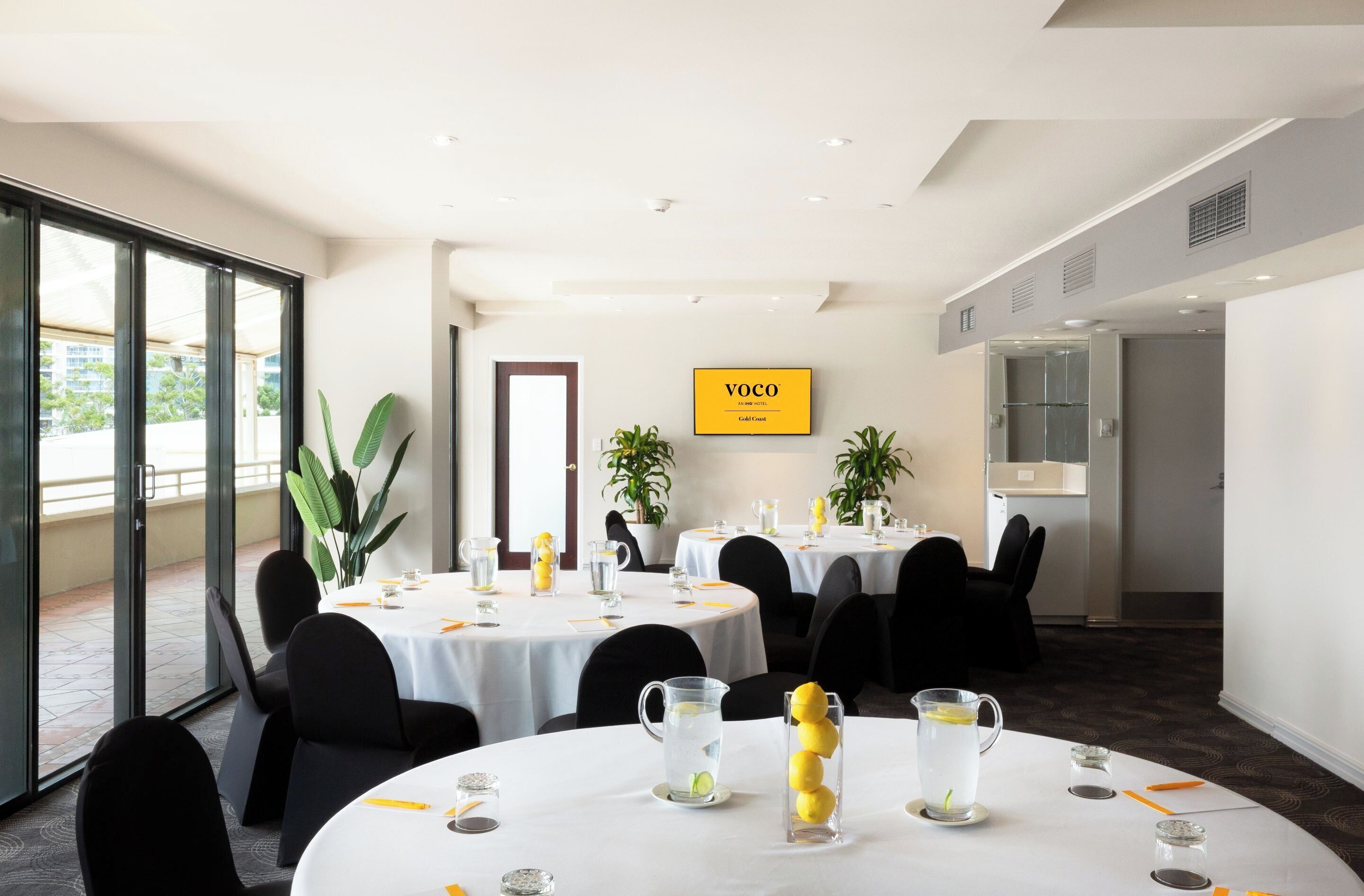 A hotel conference room with round tables, chairs, and a large window.