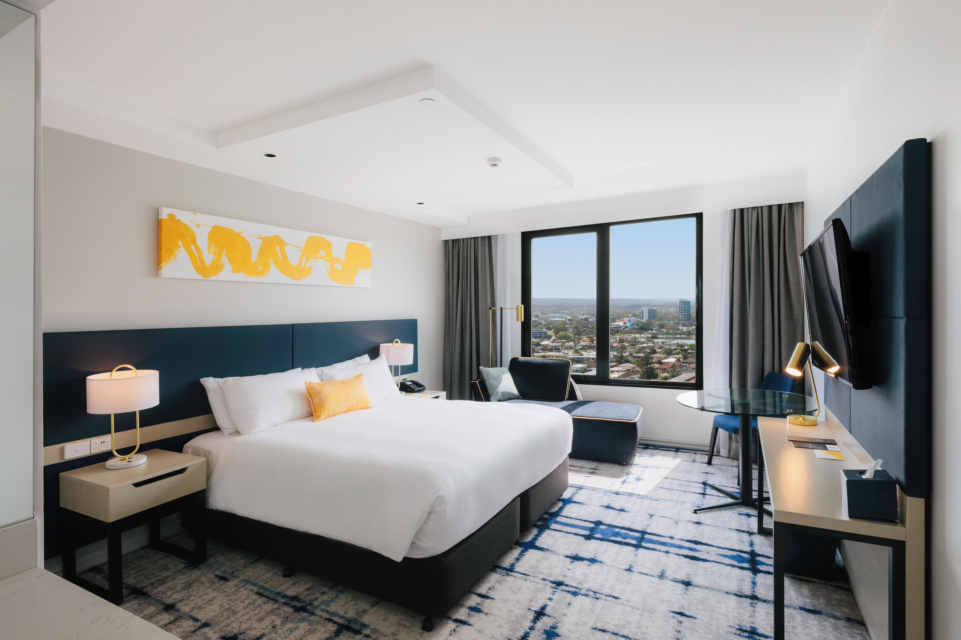 Habitación de hotel con una cama grande, un escritorio con silla, un televisor y vistas a la ciudad.