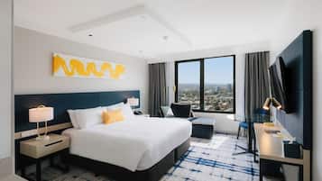 Habitación de hotel con una cama grande, un escritorio con silla, un televisor y vistas a la ciudad.