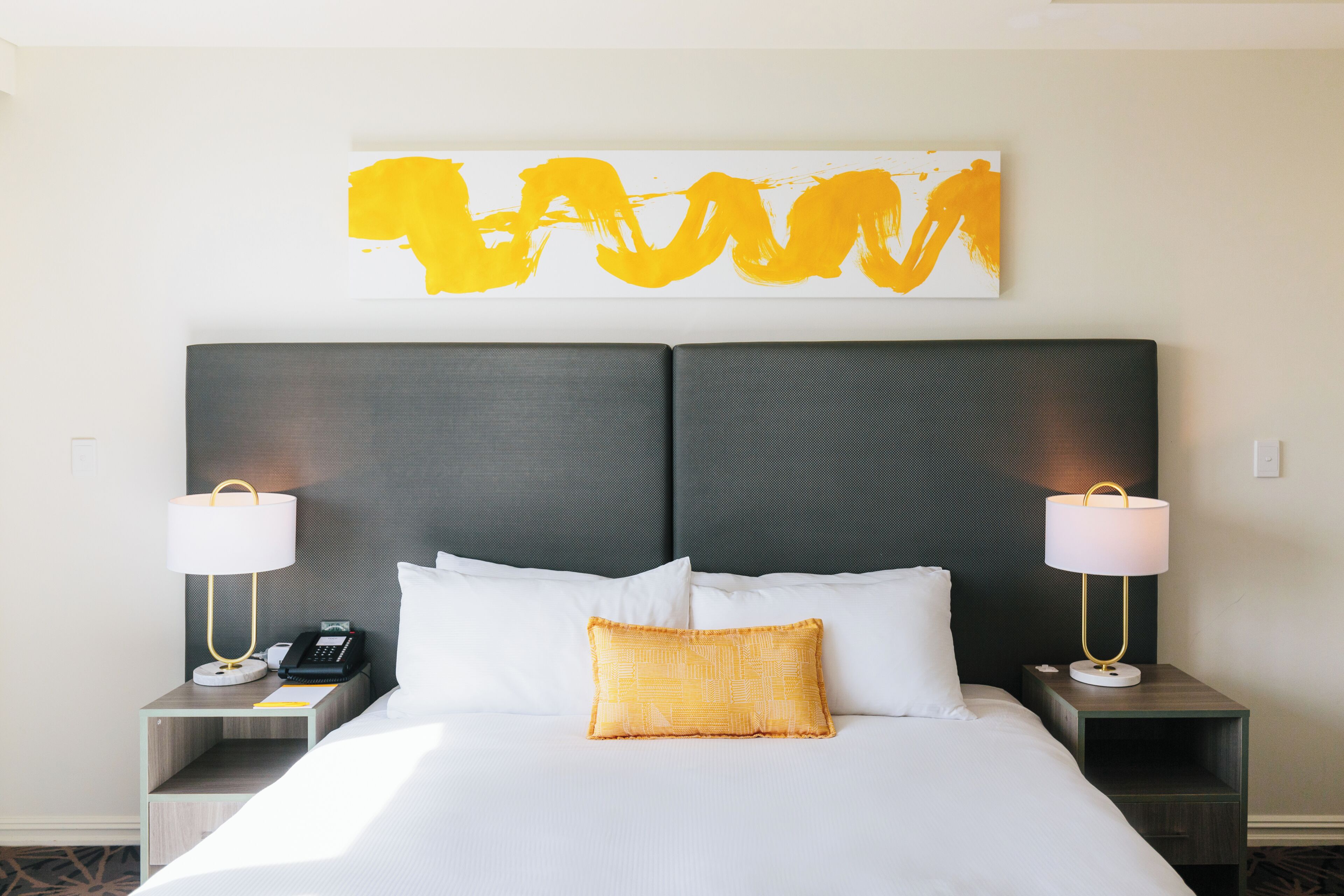 A hotel room with a large bed, two bedside tables, a wall-mounted artwork, and a nightstand with a lamp.