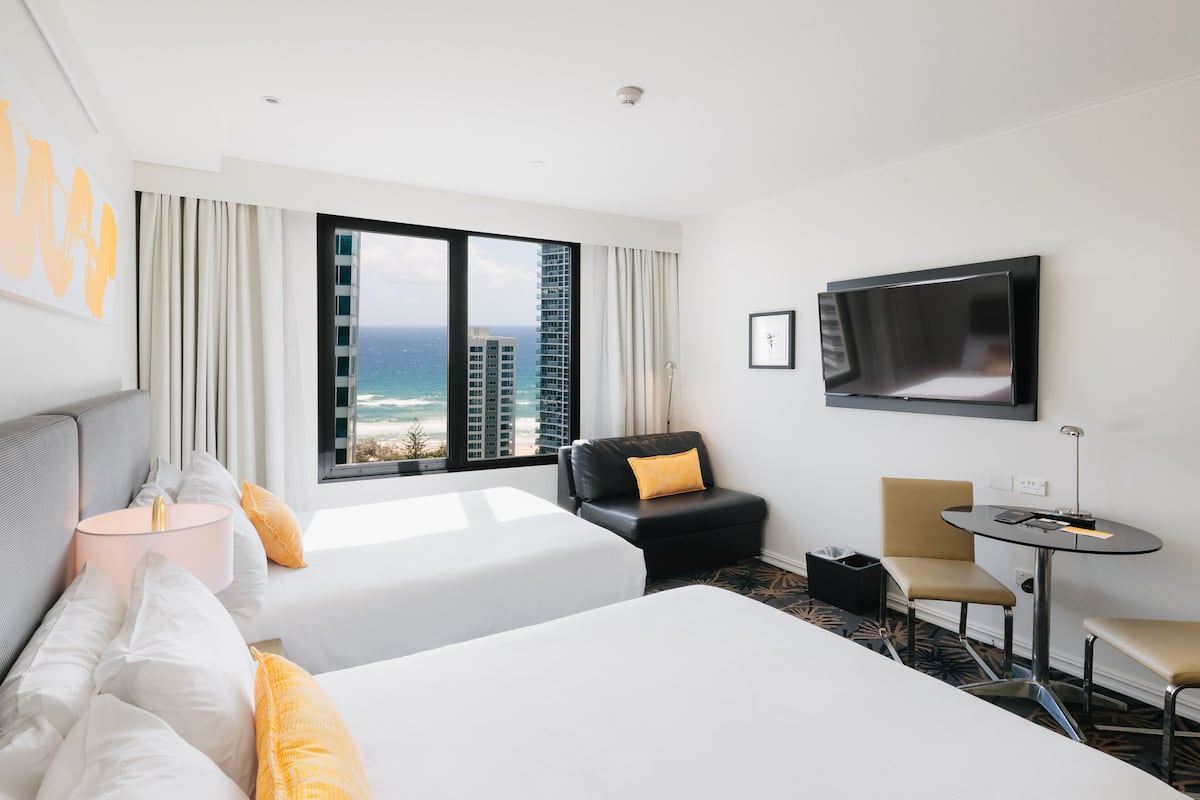 Une chambre d’hôtel avec deux lits, une télévision, un bureau et une vue sur l’océan.
