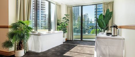 A spacious room with large windows, a white reception desk, and potted plants.