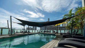 An outdoor swimming pool with lounge chairs and a cityscape in the background. - Voco Gold Coast (Surfers Paradise)