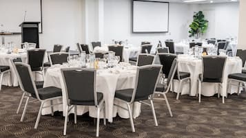 A conference room with round tables, black chairs, white tablecloths, and a projector screen.