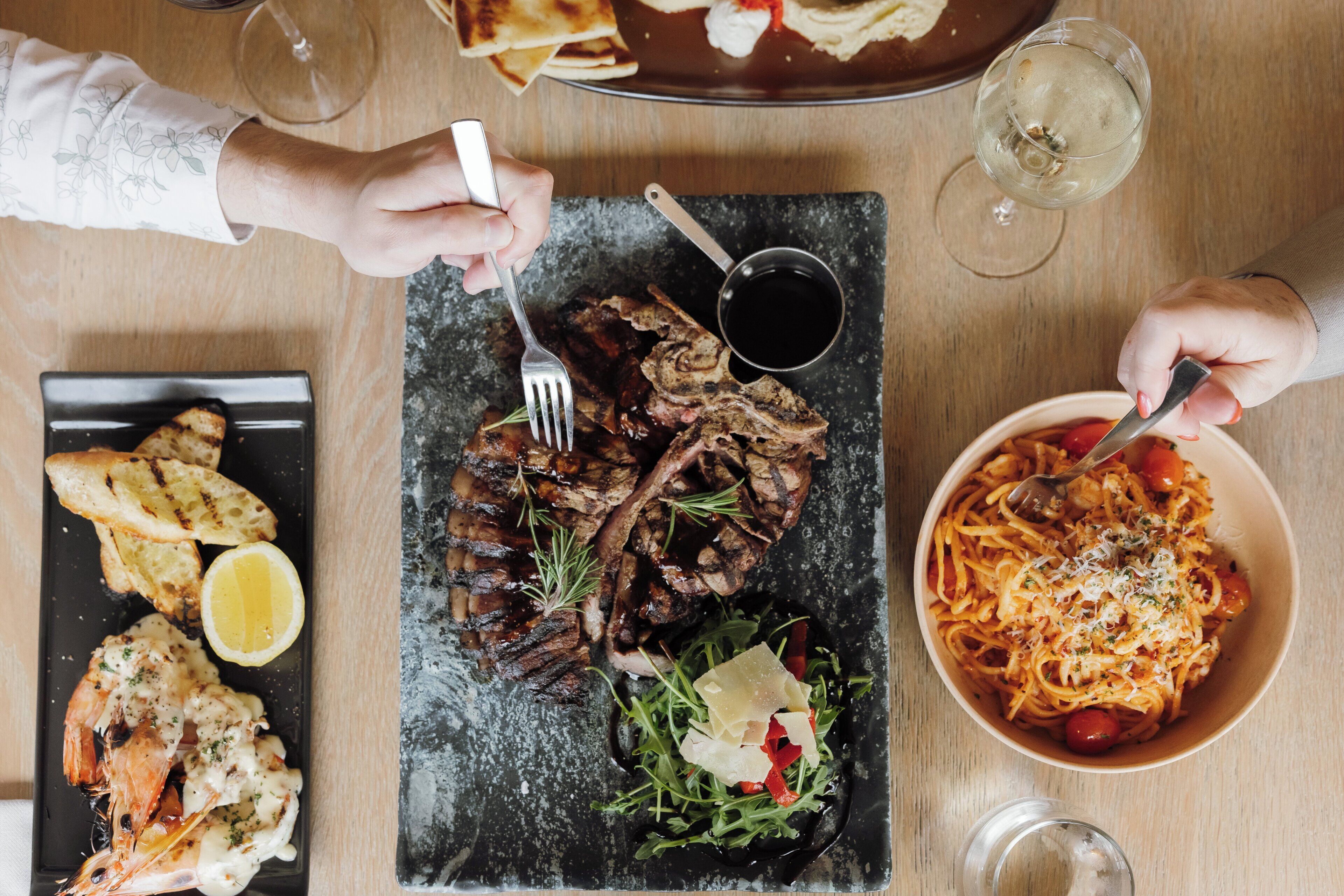 Un tavolo imbandito con diversi piatti, tra cui carne alla griglia, pasta e pane, posate e bicchieri.