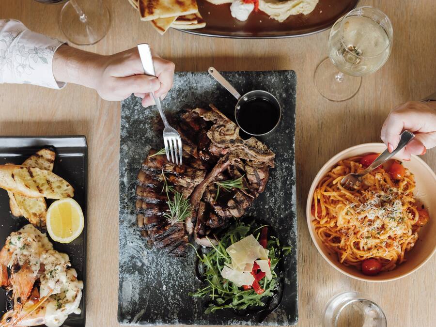 Un tavolo imbandito con diversi piatti, tra cui carne alla griglia, pasta e pane, posate e bicchieri.