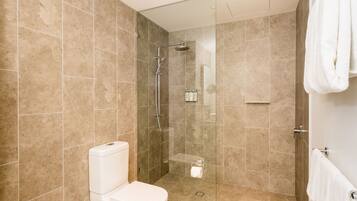 Un baño moderno con ducha envuelta en vidrio, azulejos color beige, inodoro y toallero.