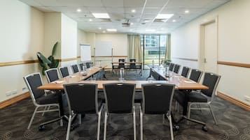 A conference room with a long table, black chairs, a whiteboard, and a plant.