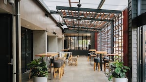 An outdoor cafe with tables and chairs, potted plants, and a wooden pergola. - Voco Gold Coast (Surfers Paradise)