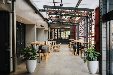 An outdoor cafe with tables and chairs, potted plants, and a wooden pergola.