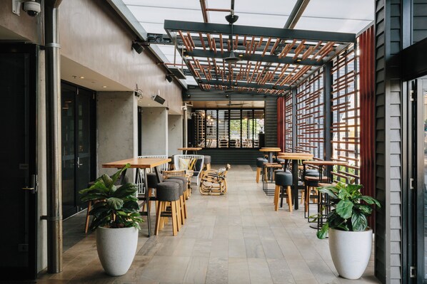 An outdoor cafe with tables and chairs, potted plants, and a wooden pergola. - Voco Gold Coast (Surfers Paradise)