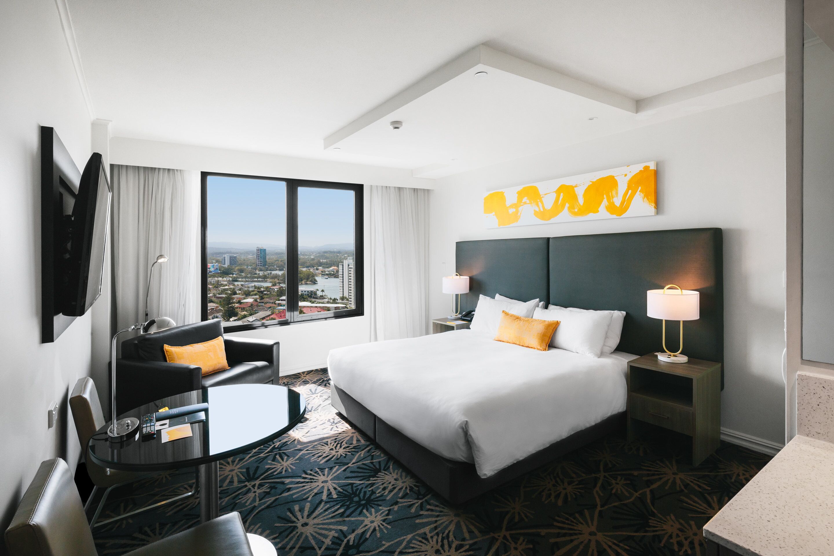 A hotel room with a large bed, a desk, a chair, a view of the city, and a modern design.