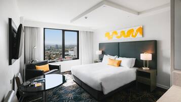 A hotel room with a large bed, a desk, a chair, a view of the city, and a modern design.
