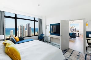 Habitación de hotel con una cama grande, un escritorio con silla, televisión y vistas a la ciudad y al océano.