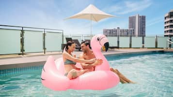 Guests can enjoy a refreshing swim in the pool surrounded by a glass railing and shaded by an umbrella.